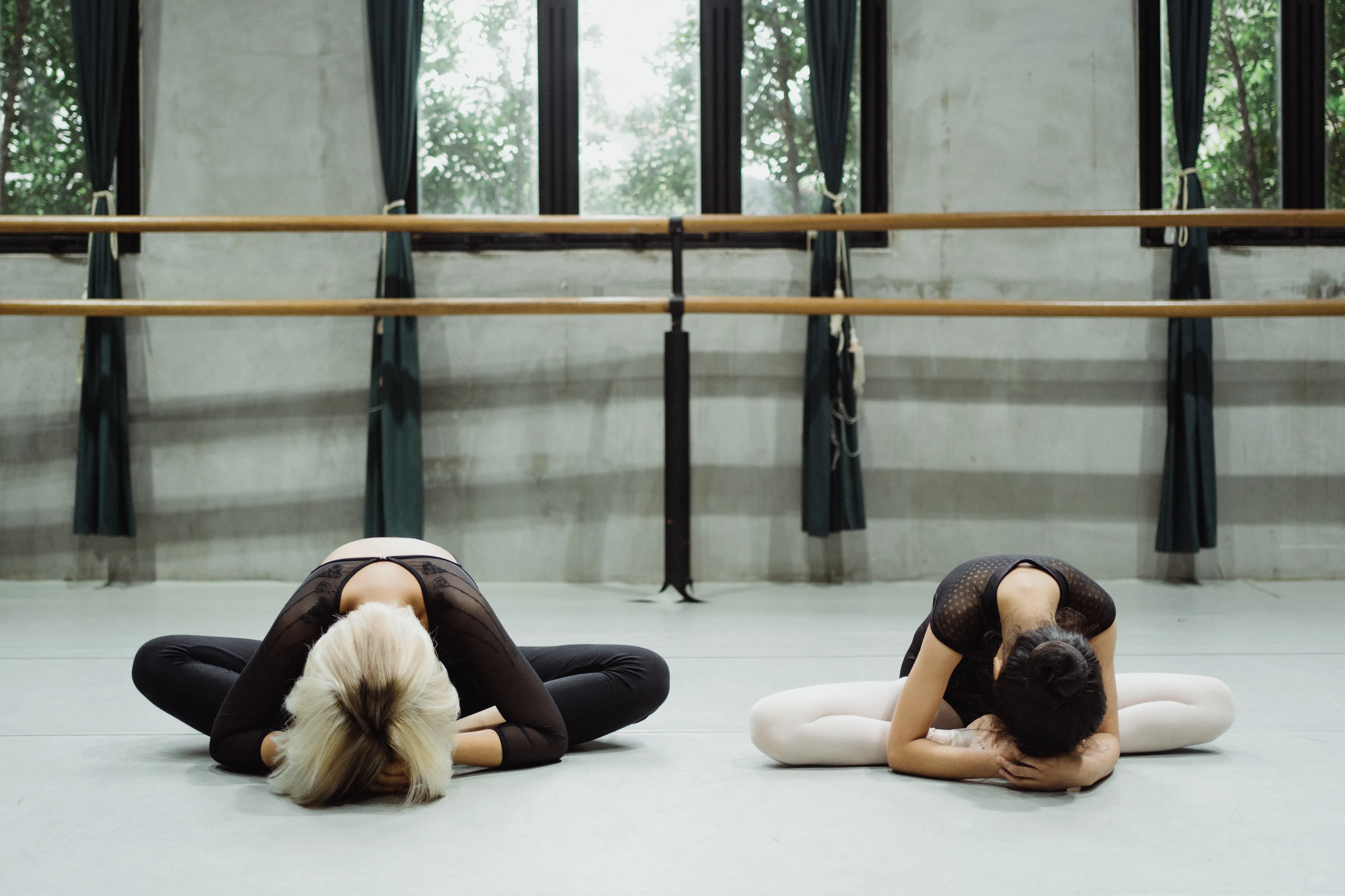 An instructor guides a student through a stretch at the barre in a daylit studio